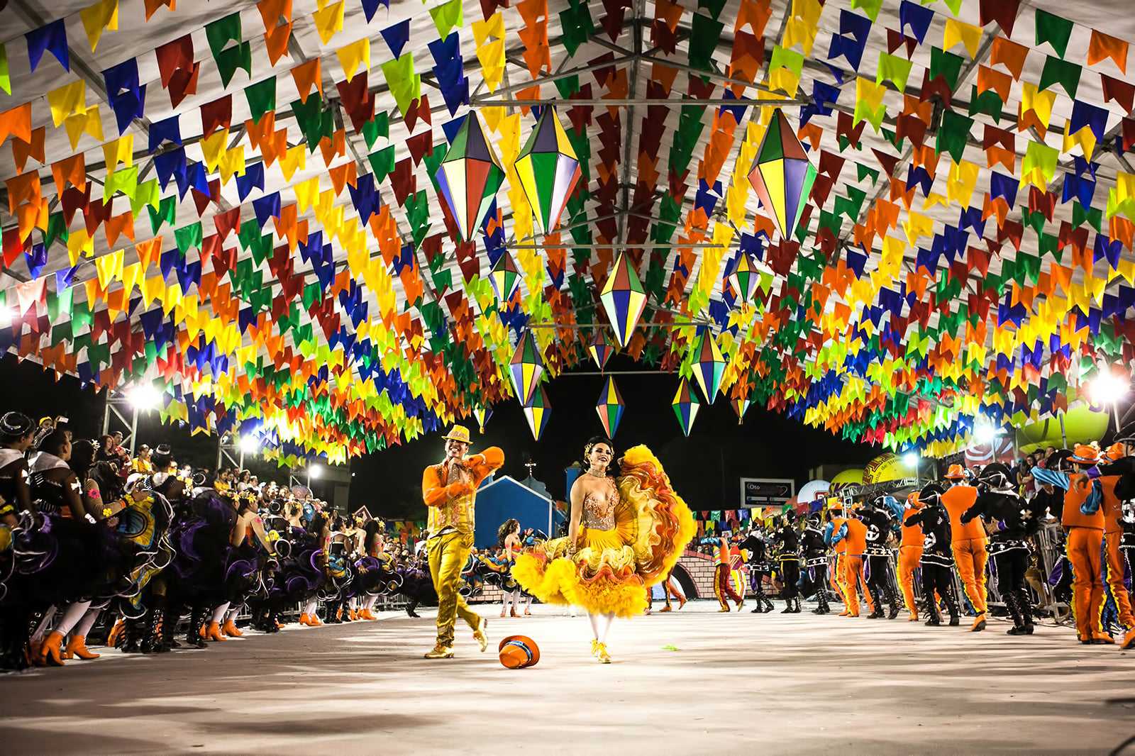 Apresentação de quadrilha em Caruaru com figurinos coloridos e público em arquibancadas cobertas